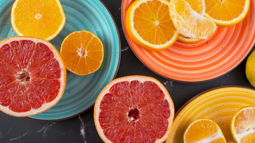 Top view of sliced citrus fruits on multicolored plates, featuring oranges, grapefruit, and mandarins.