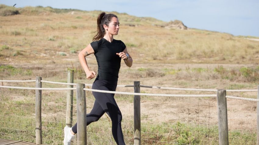 Woman jogging on a sunny day on a wooden path in Portugal, embracing a healthy lifestyle.